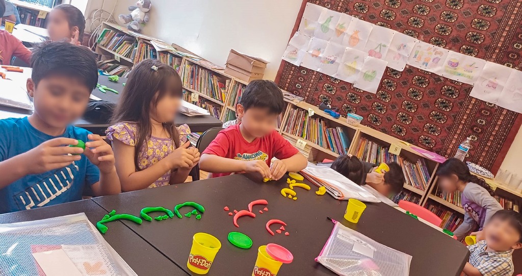 A group of young children use playdough to form farsi letters.